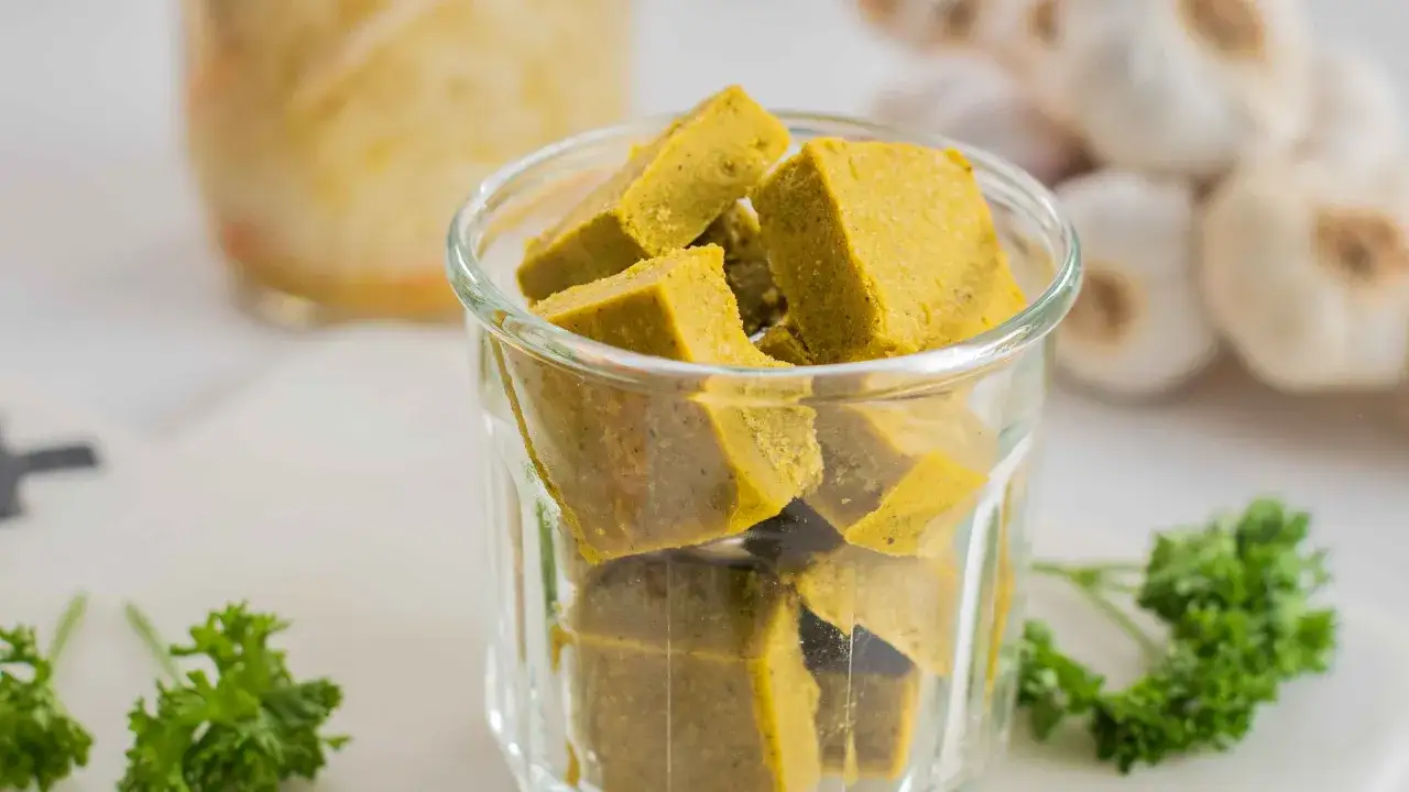Un verre rempli de cubes de bouillon maison, avec de l'ail et du persil en arrière-plan.