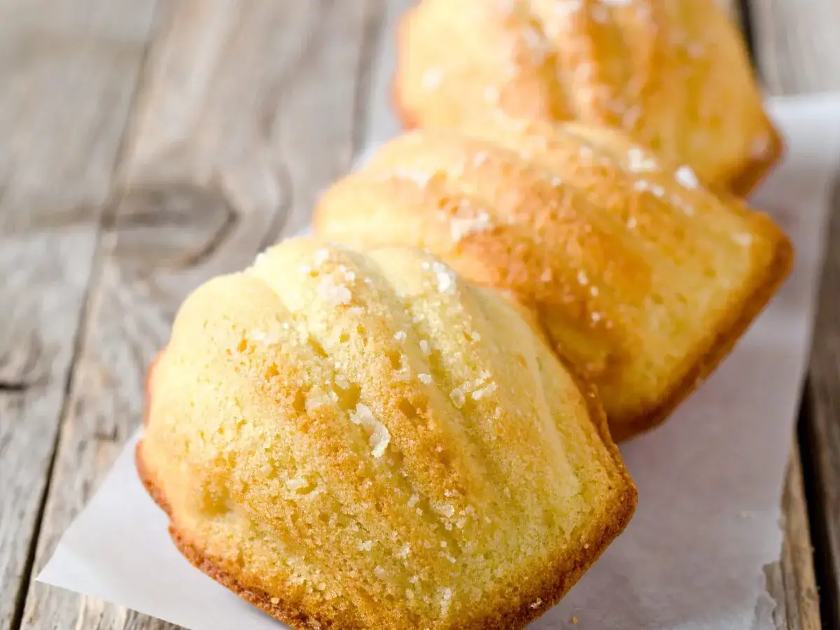 Trois madeleines salées originales, dorées et saupoudrées de gros sel, sur un fond de bois vieilli.