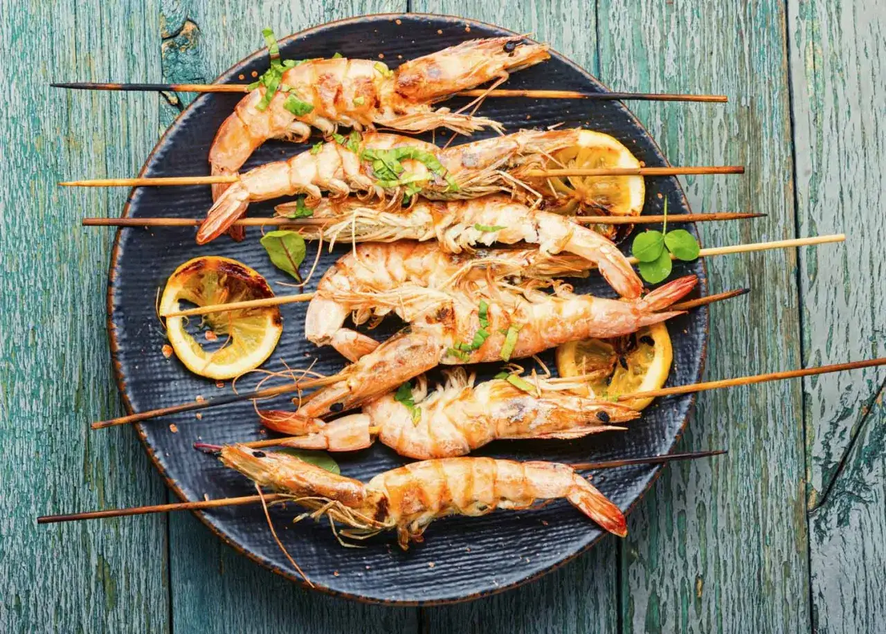 Langoustines grillées sur brochettes, garnies d'herbes fraîches et de quartiers de citron. Un délice de langoustine barbecue prêt à être dégusté.