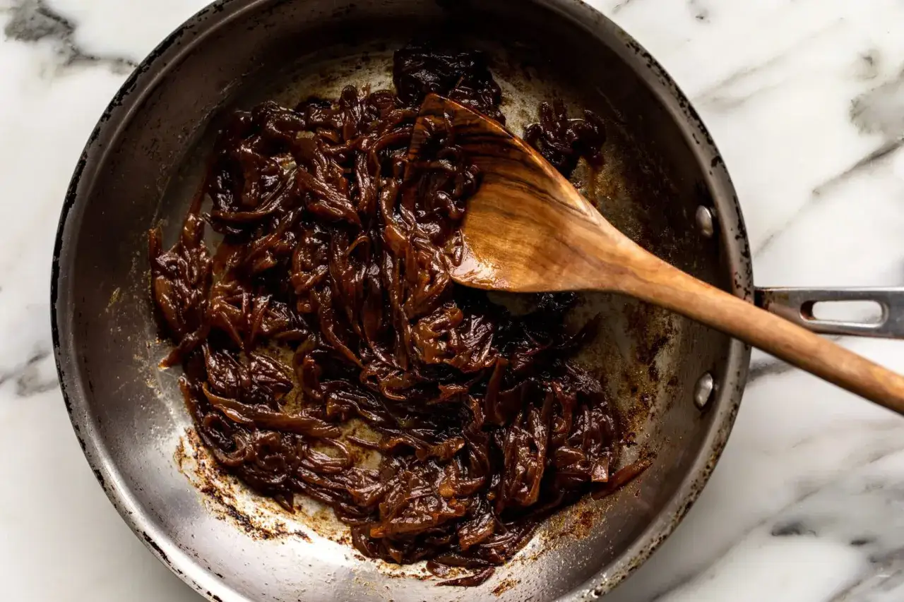 Cuillère en bois remuant des oignons caramélisés dans une poêle, prêts à deglacer oignons pour une sauce riche.
