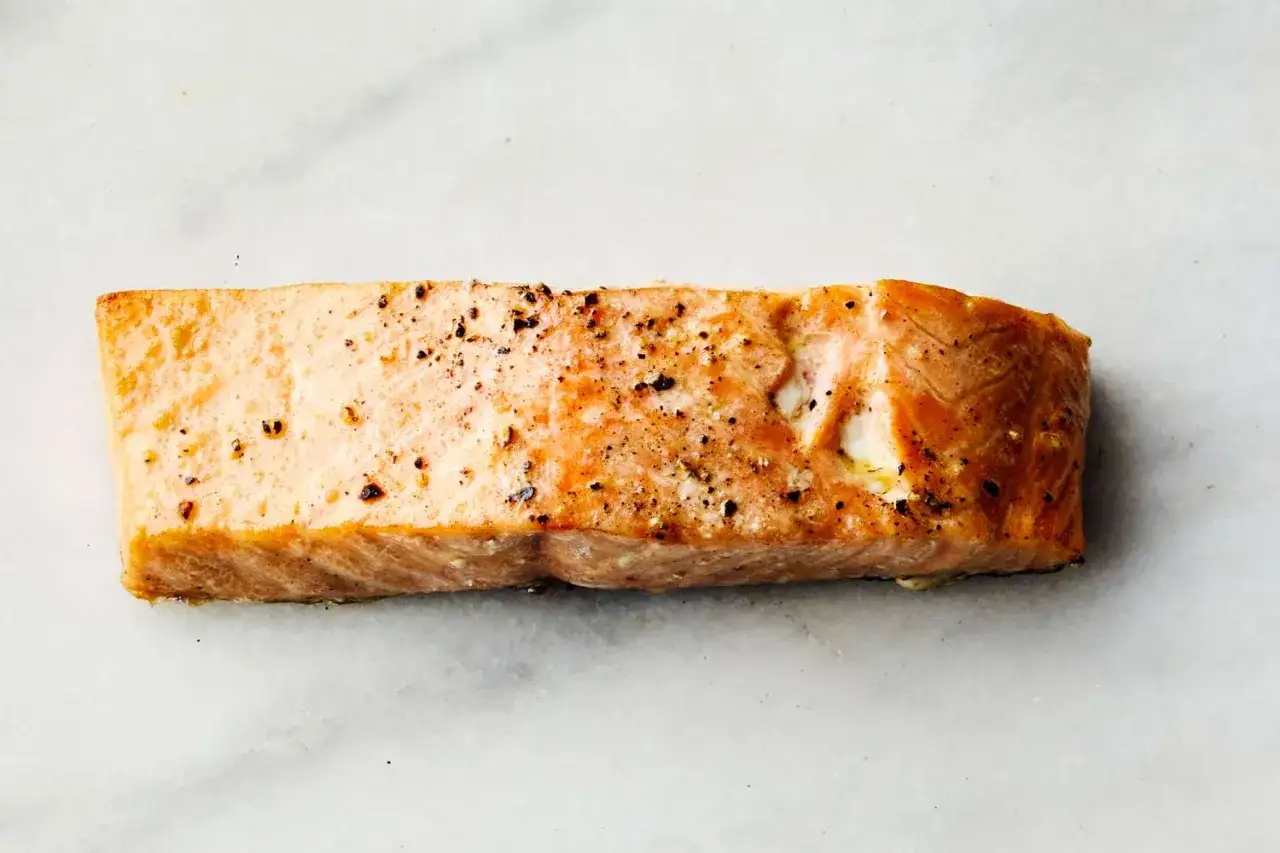 Un morceau de saumon parfaitement cuit, assaisonné de poivre noir, prêt pour la cuisson.