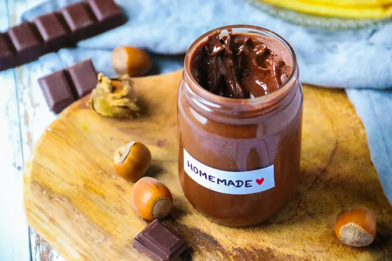 P&acirc;te &agrave; tartiner maison, onctueuse et chocolat&eacute;e, rappelant le go&ucirc;t du Kinder Bueno. Des noisettes et des carr&eacute;s de chocolat compl&egrave;tent la sc&egrave;ne gourmande.