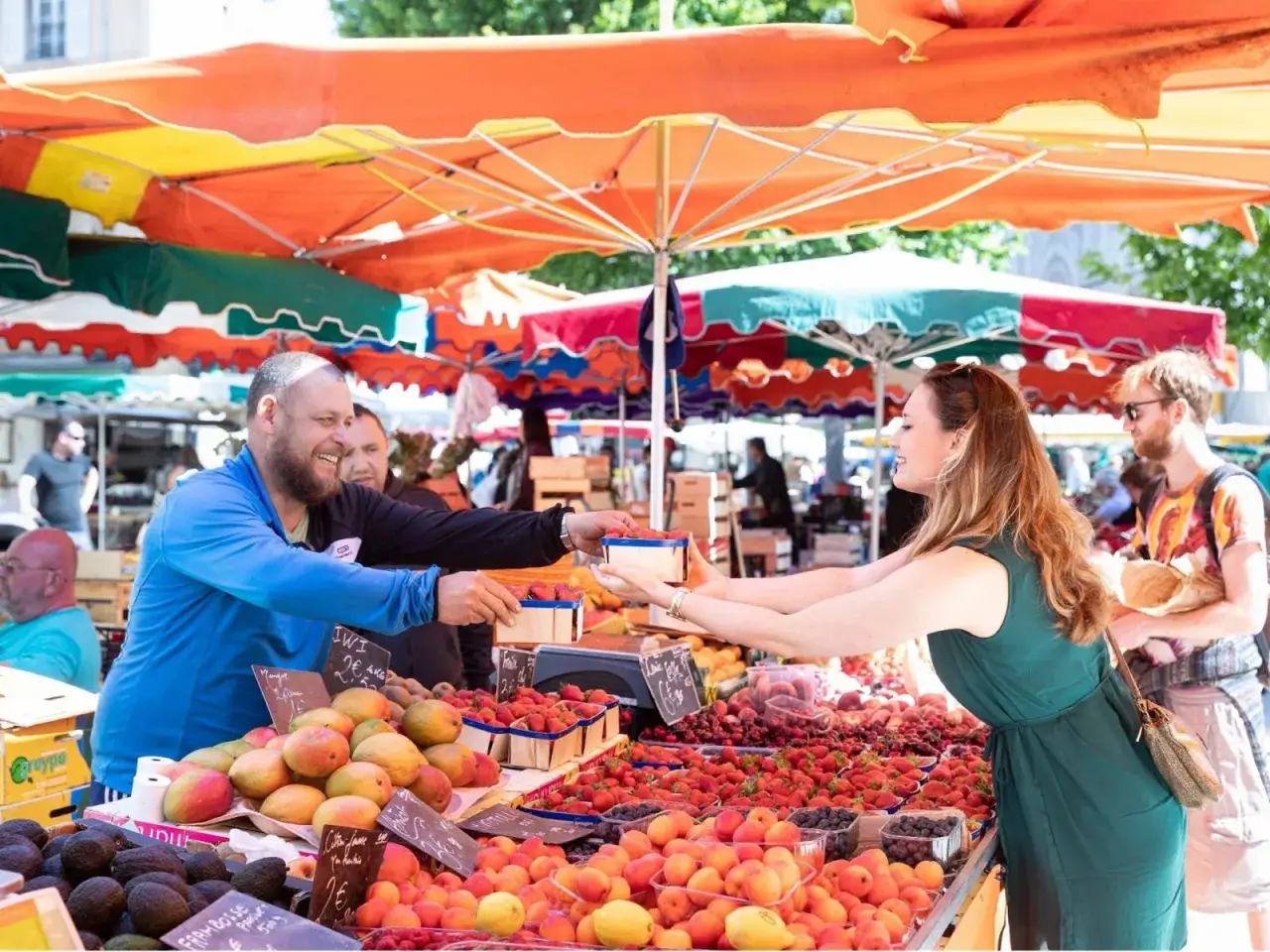 Un vendeur souriant tend des fraises à une cliente sur un marché d'été. Fruits et légumes de saison, un vrai régal de juillet.
