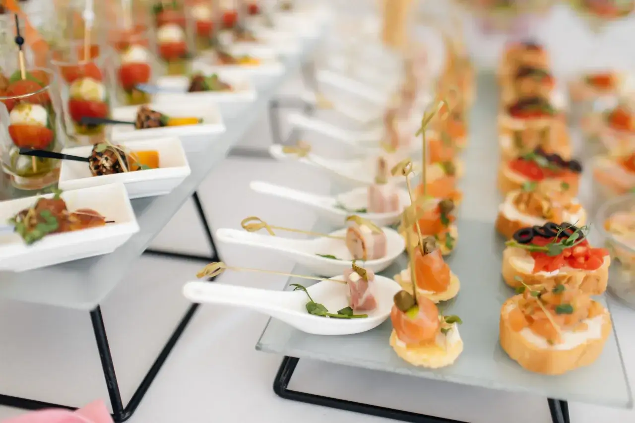 Un buffet de mariage élégant avec des amuse-bouches variés : brochettes de tomates et mozzarella, roulés de jambon, toasts au saumon et olives.