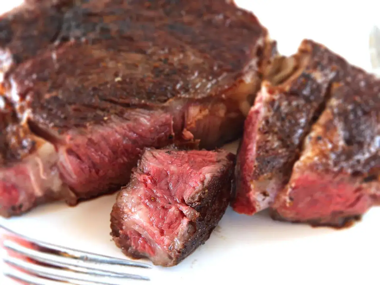 Un steak parfaitement cuit, avec une croûte dorée et une chair rosée, résultat d'une cuisson reverse sear. Une fourchette est visible.