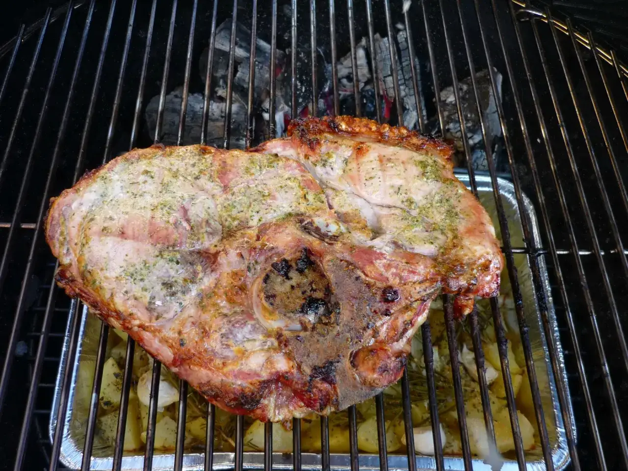 Une rouelle de porc au barbecue, assaisonnée d'herbes, cuit sur des pommes de terre et de l'ail dans une barquette en aluminium.