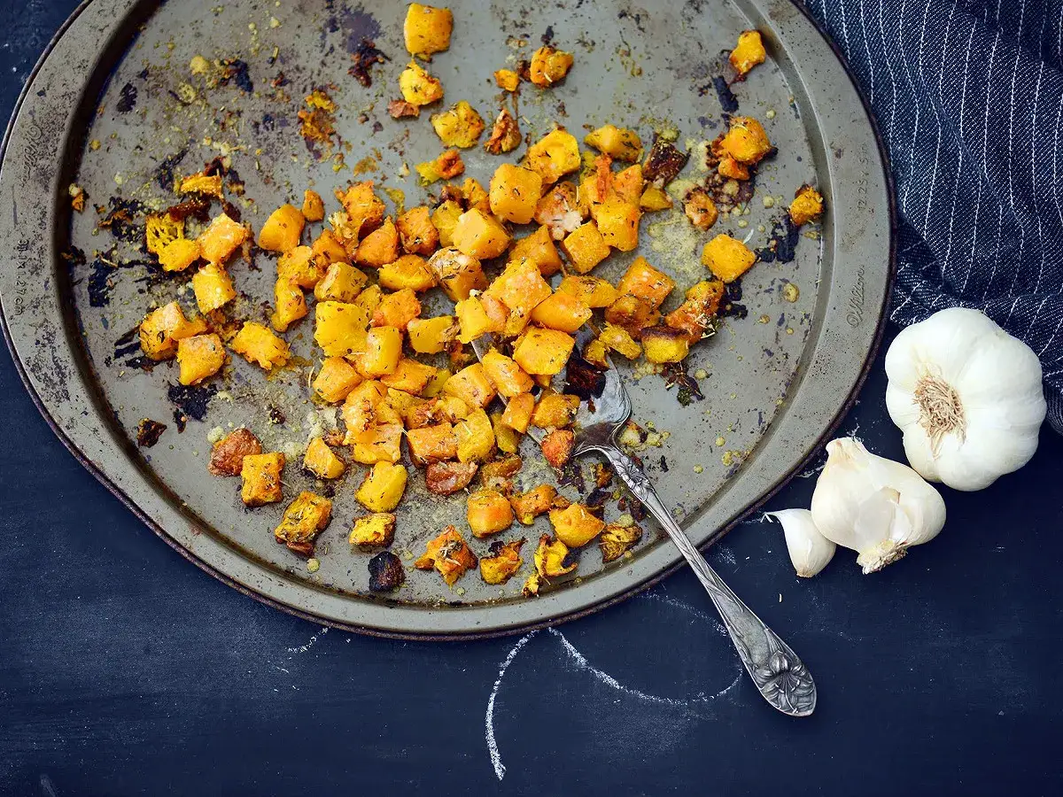 Désormais, le butternut braisé est prêt à être dégusté. Des morceaux dorés sur une plaque, accompagnés d'ail et d'une serviette.