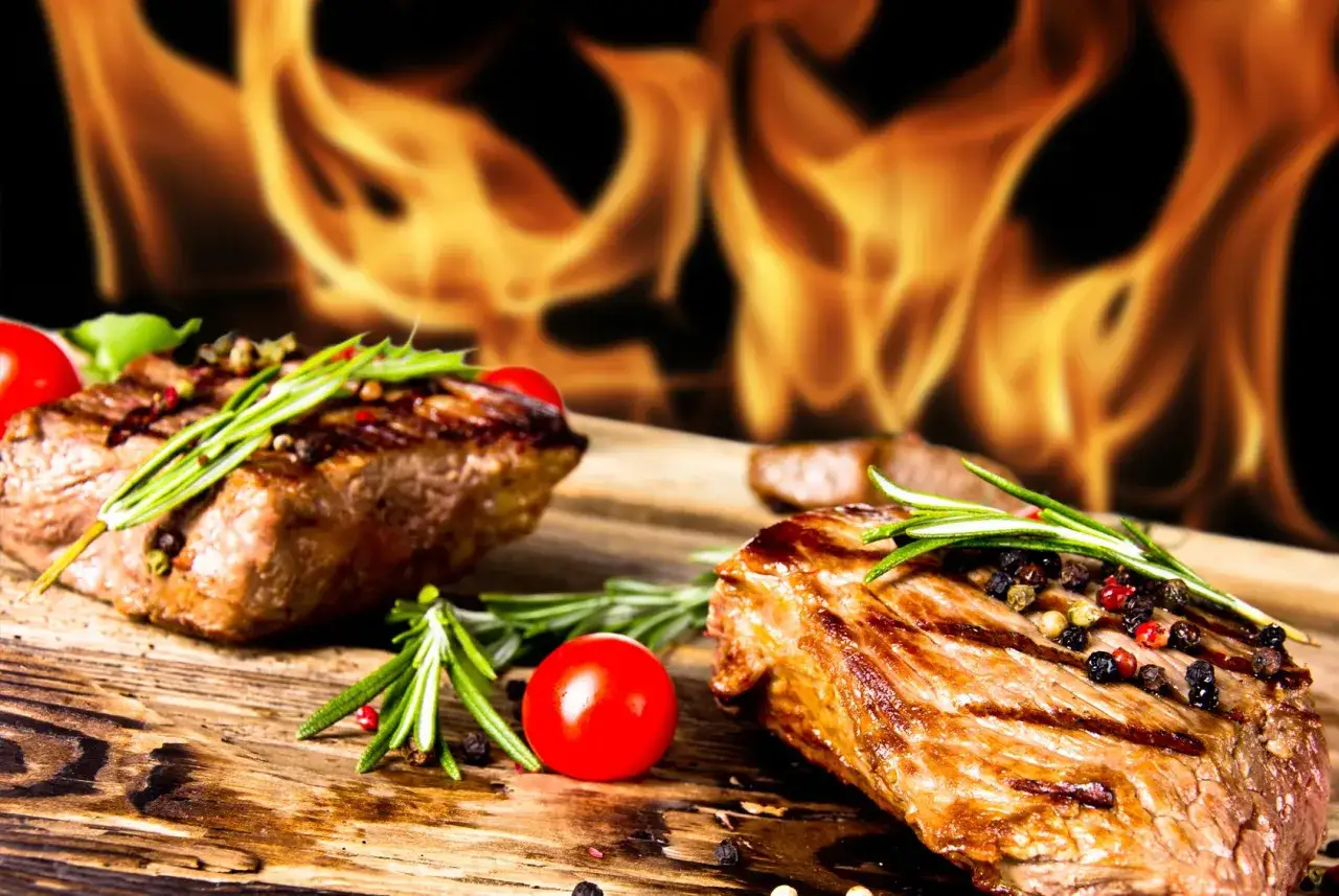Deux côtes de bœuf grillées au feu de bois, garnies de romarin et de poivre, sur une planche en bois.
