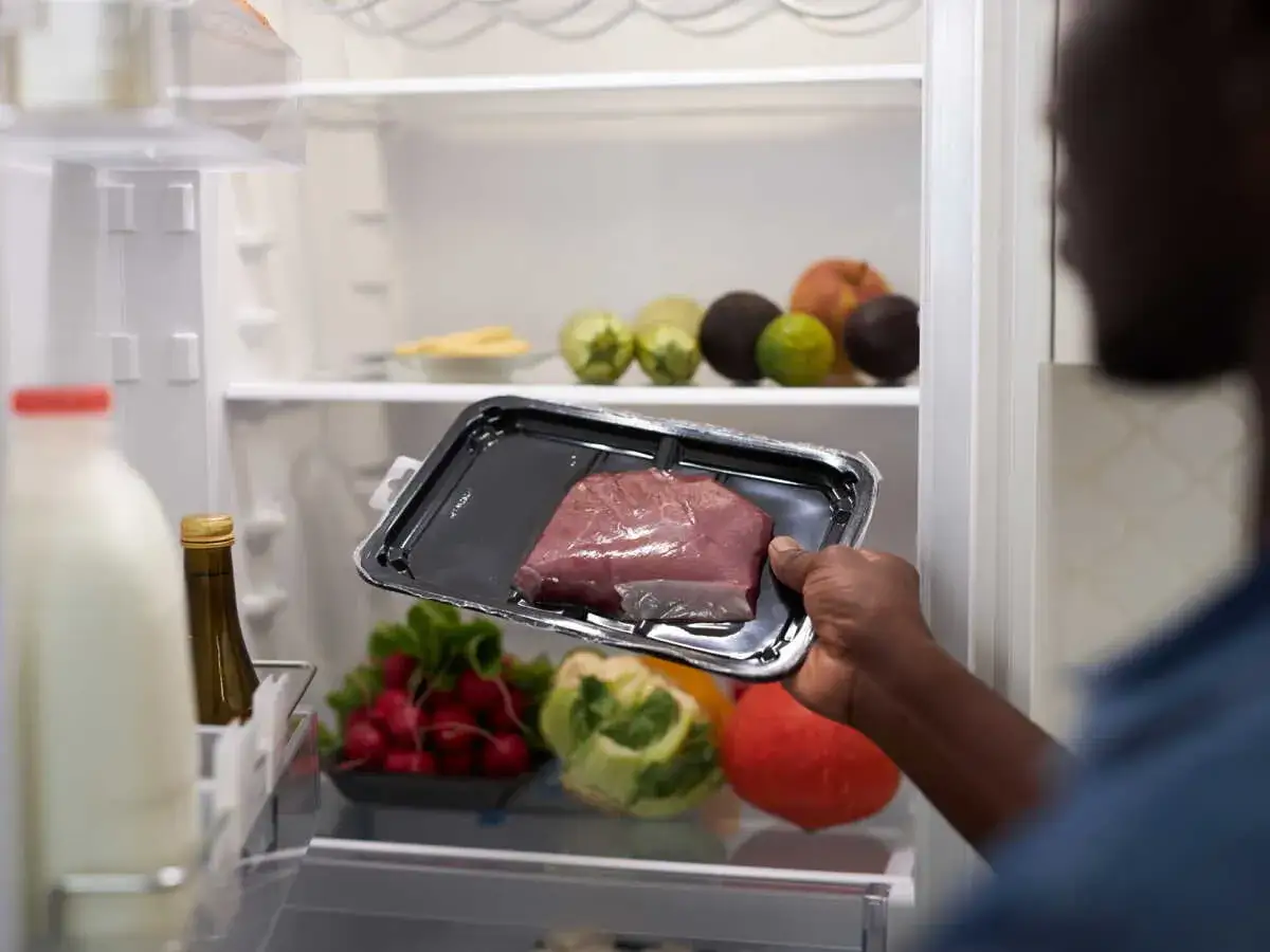 Un homme regarde un morceau de viande dans son emballage. Il se demande : viande hors frigo combien de temps ?
