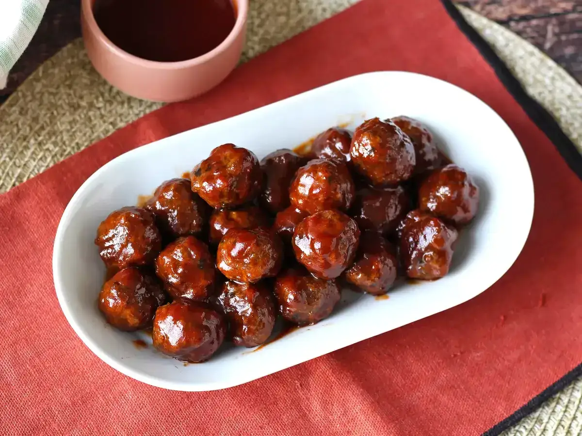 Un plat blanc rempli de boulettes de viande barbecue, nappées d'une sauce savoureuse. Parfaites pour un apéritif ou un repas convivial.