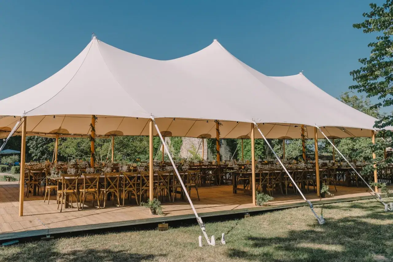 Grande tente blanche dressée pour un mariage chez soi, tables dressées et chaises en bois attendent les invités sous un ciel bleu.