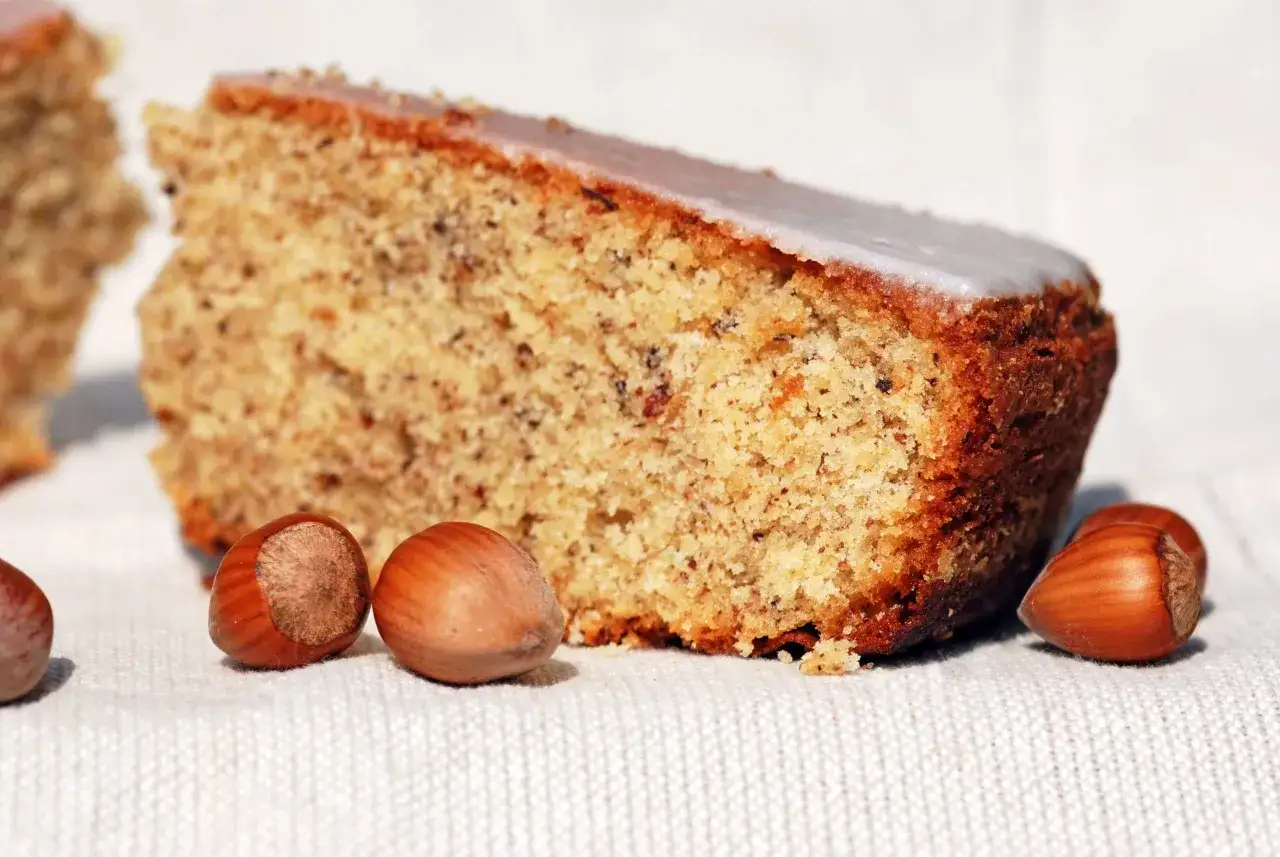 Une part de gâteau moelleux aux noisettes de ma mamie, avec quelques noisettes entières posées à côté.