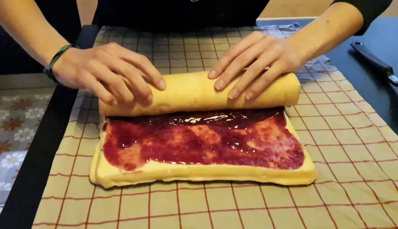 Préparation d'une recette génoise bûche moelleuse : on roule délicatement le biscuit garni de confiture.