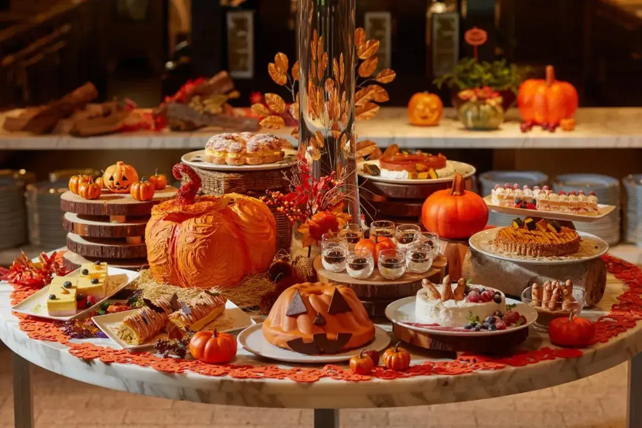 Buffet d'Halloween avec des desserts en forme de citrouille, des gâteaux et des crudités.