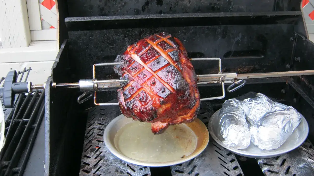 Jambon &agrave; la broche pour 50 personnes, dor&eacute; et grill&eacute;, avec des pommes de terre en papillote sur le c&ocirc;t&eacute;.