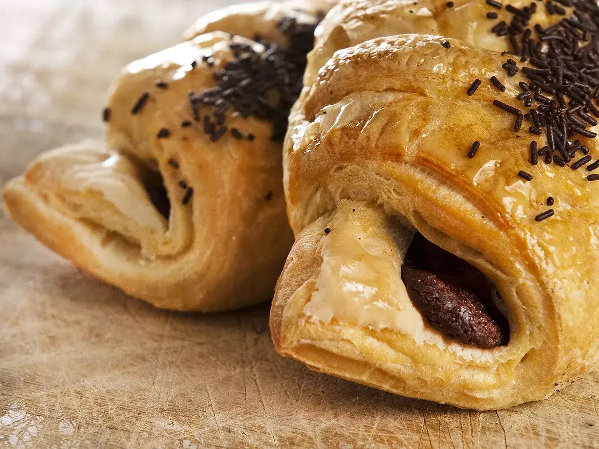 Deux croissants au chocolat en pâte feuilletée, saupoudrés de vermicelles, sur une planche en bois.
