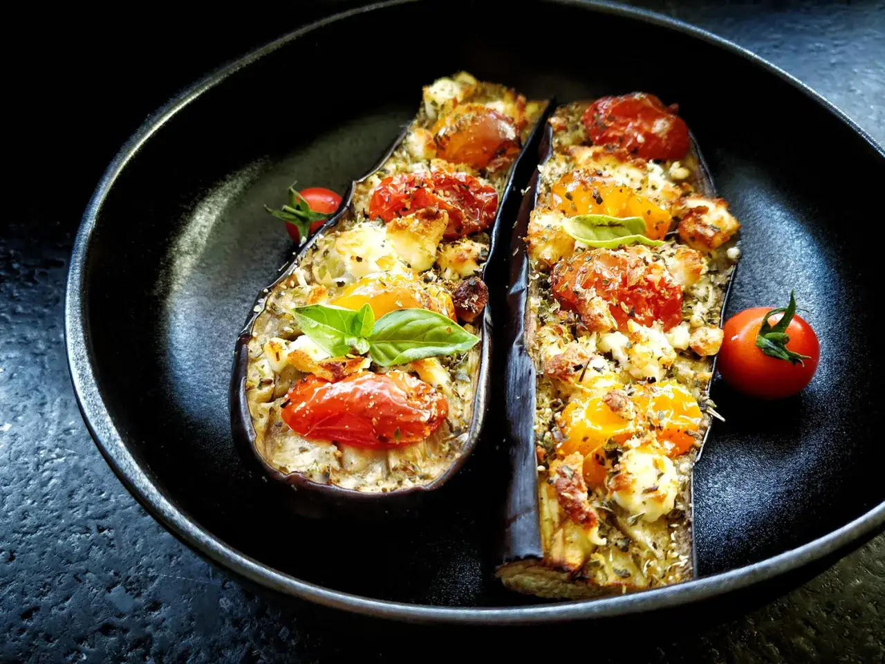 Deux moitiés d'aubergine farcies de tomates, fromage et herbes, dans une poêle. Une idée pour que faire avec 1 aubergine.