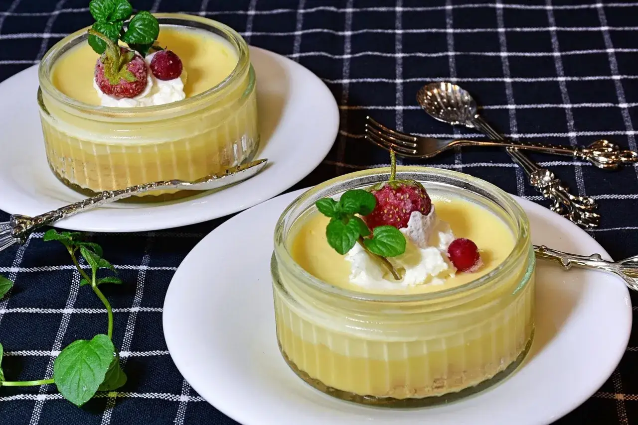 Deux flans au citron crémeux, garnis d'une fraise, d'une baie rouge et de menthe, prêts à être dégustés.