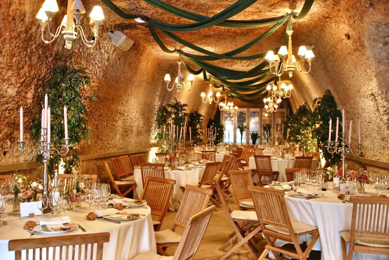 Une salle de réception rustique, décorée de draperies vertes et de lustres, prête pour une formule pour un mariage. Tables dressées, bougies et verdure créent une ambiance chaleureuse.