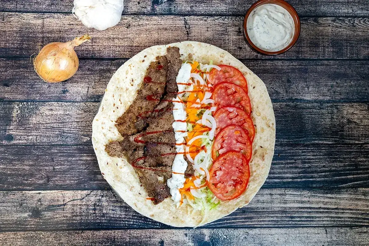 Un kebab maison facile garni de viande, tomates, oignons, salade et sauce blanche. Un délice à portée de main !
