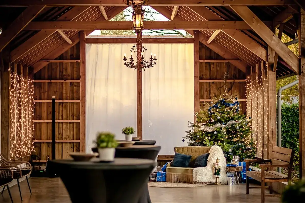 Une ambiance chaleureuse pour un mariage en hiver : sapin décoré, guirlandes lumineuses et mobilier cosy dans une grange en bois.