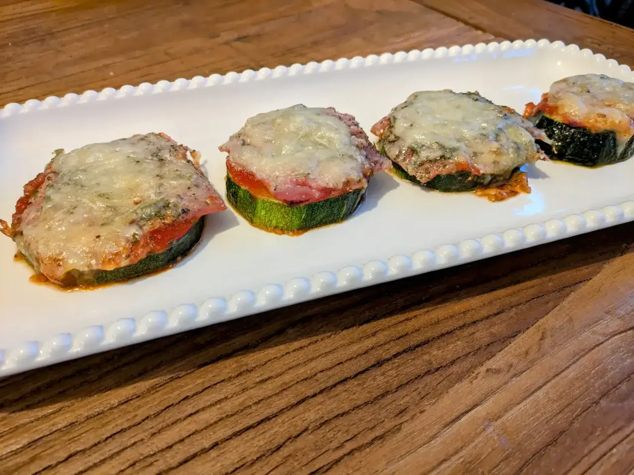 Quatre rondelles de courgette façon pizza, garnies de sauce tomate, jambon et fromage fondu, servies sur un plat blanc.
