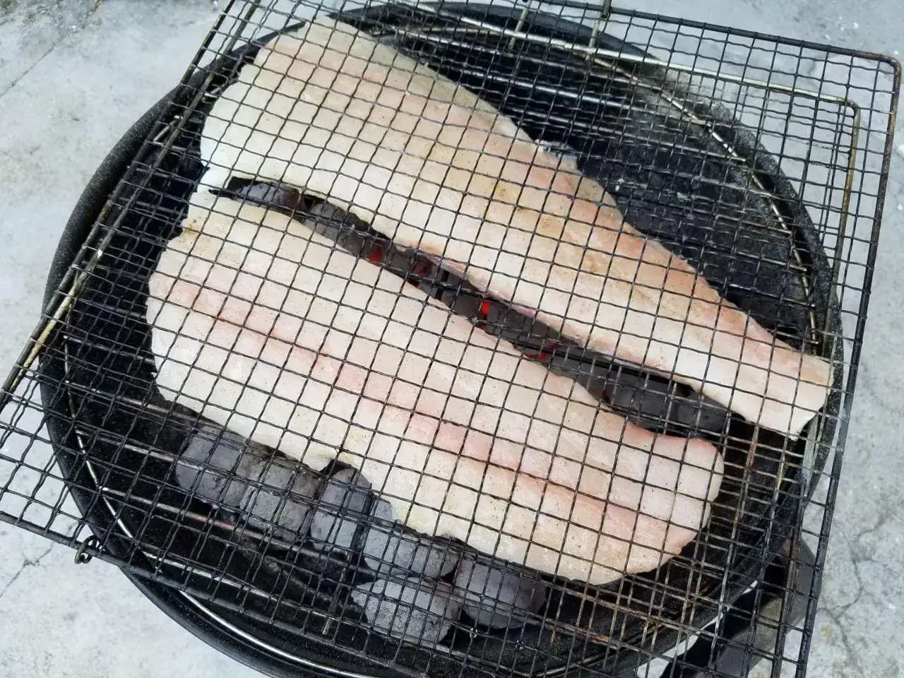 Deux filets de cabillaud au barbecue, pr&ecirc;ts &agrave; &ecirc;tre grill&eacute;s sur des braises ardentes.