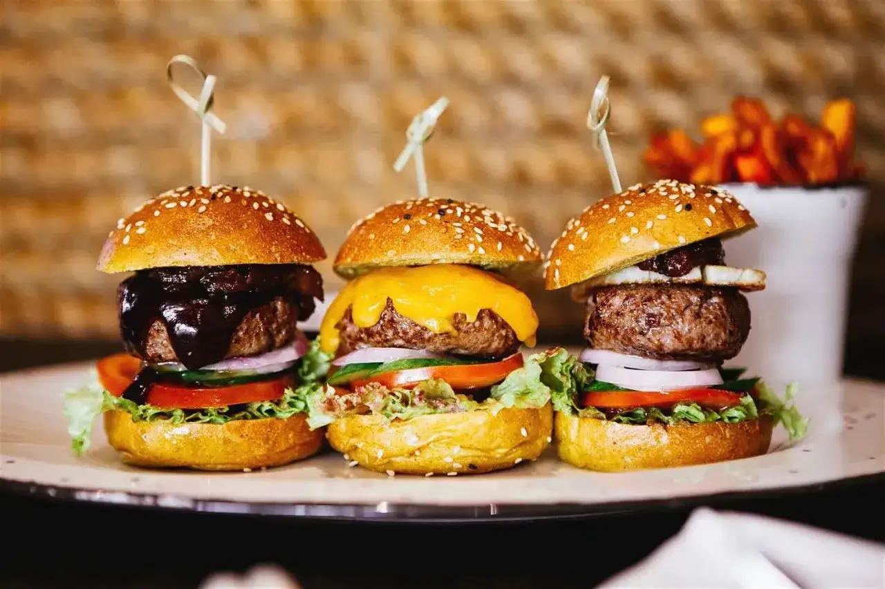 Trois mini burgers app&eacute;tissants, parfaits pour un burger enfant, pr&eacute;sent&eacute;s sur une assiette avec des frites en arri&egrave;re-plan.