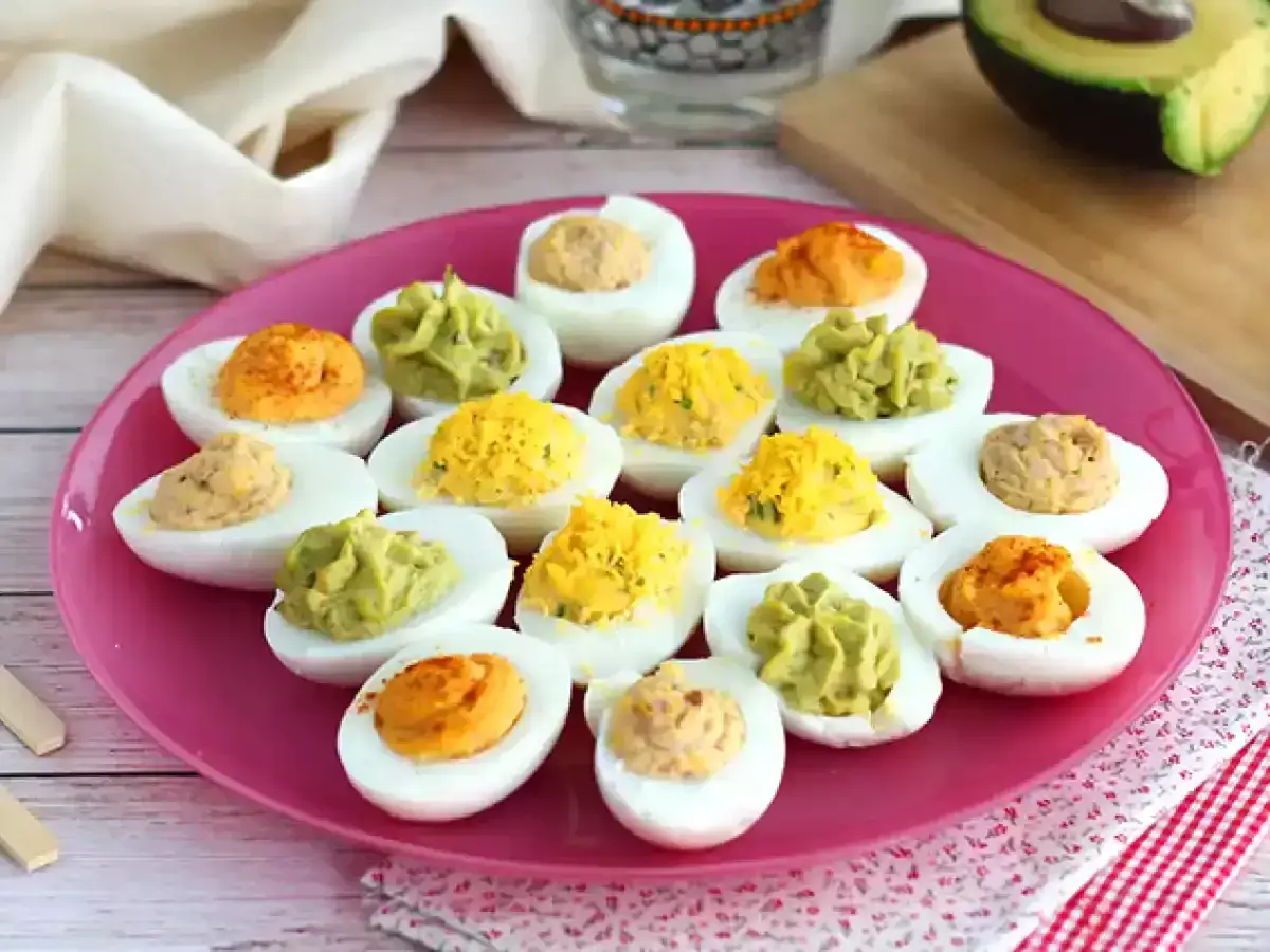 Assiette rose remplie d'oeufs durs déguisés aux garnitures variées : avocat, paprika, et jaune d'oeuf.