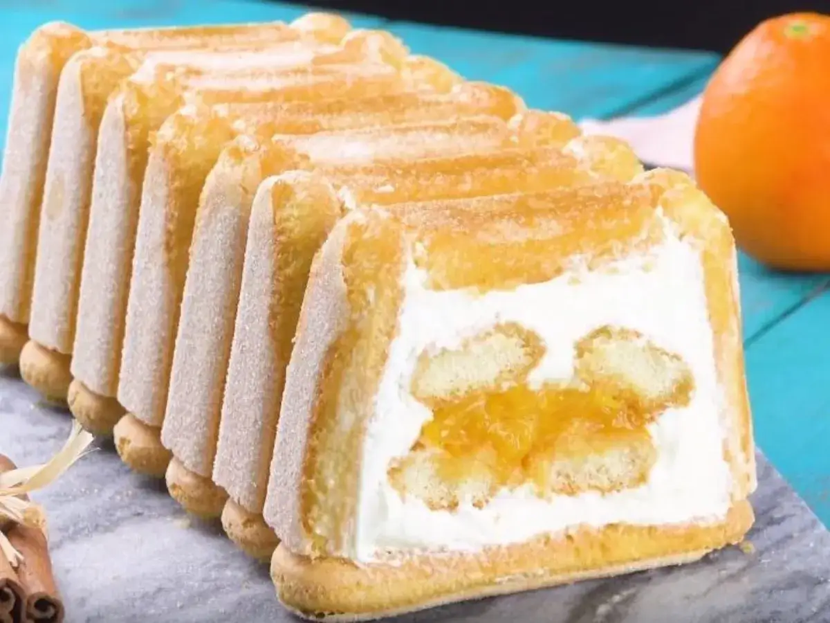 Une délicieuse charlotte à l'orange, garnie de crème et de morceaux d'orange confite, entourée de biscuits à la cuillère saupoudrés de sucre.