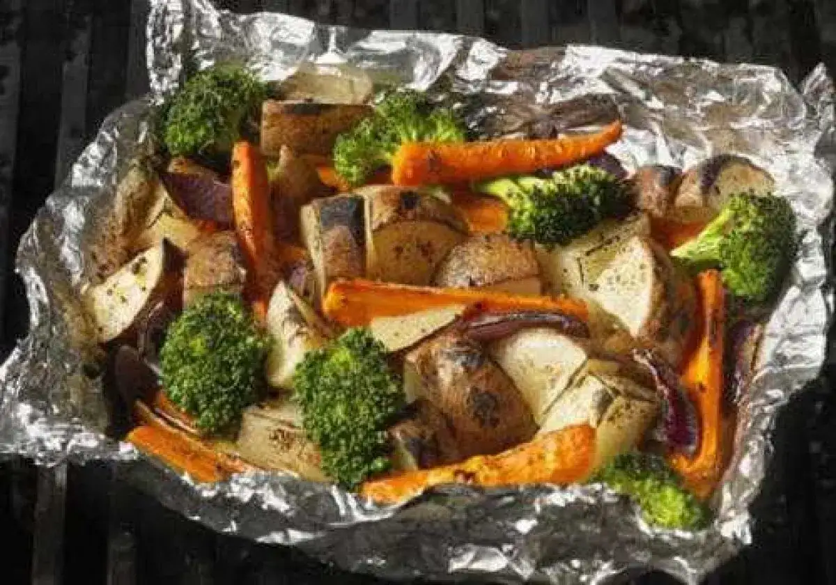 Légumes variés (pommes de terre, carottes, brocolis, oignons rouges) cuits en papillote sur un barbecue, prêts à être dégustés.