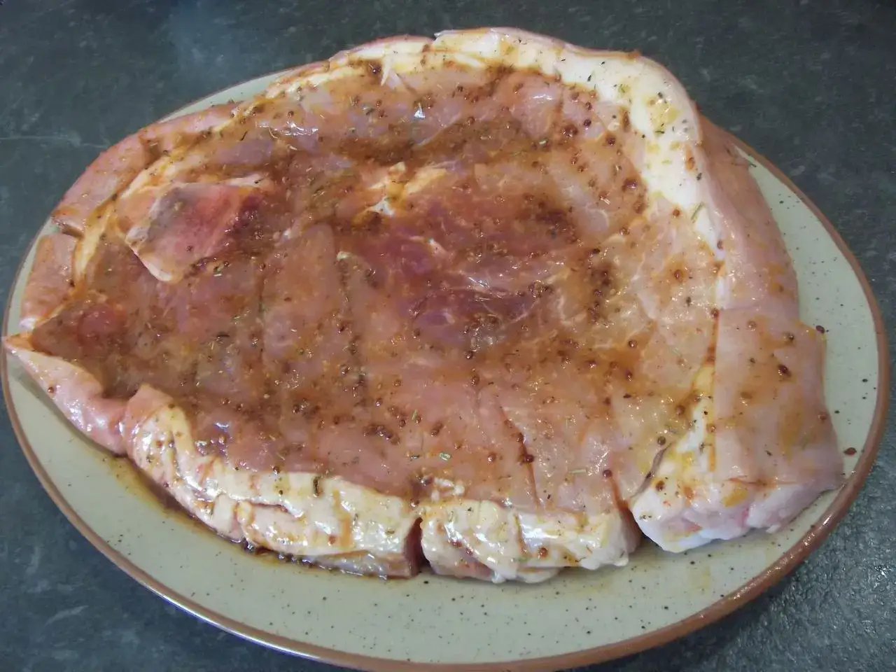 Rouelle de porc crue, prête pour la plancha, généreusement recouverte d'une marinade aux herbes et épices.