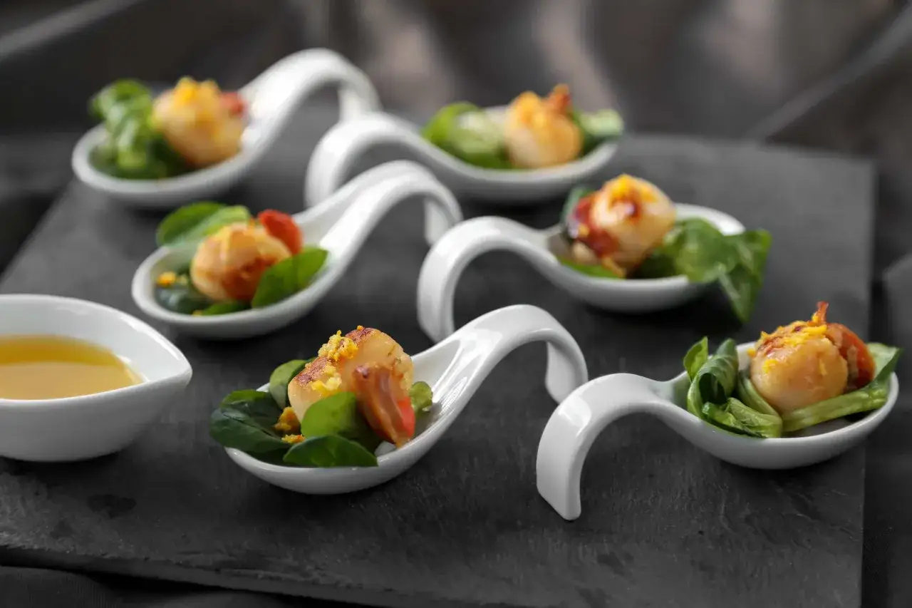 D&eacute;licieuses saint jacques au barbecue, servies sur des cuill&egrave;res blanches avec des feuilles vertes et une touche de tomate. Un d&eacute;lice &agrave; savourer !