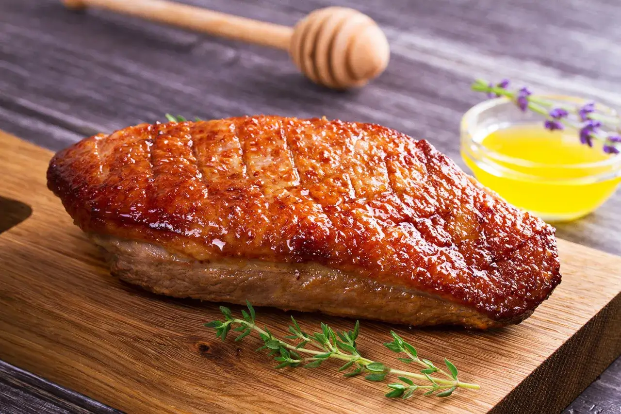 Magret de canard grillé, peau croustillante, prêt pour la cuisson au barbecue gaz. Servi avec une sauce dorée et des herbes fraîches.