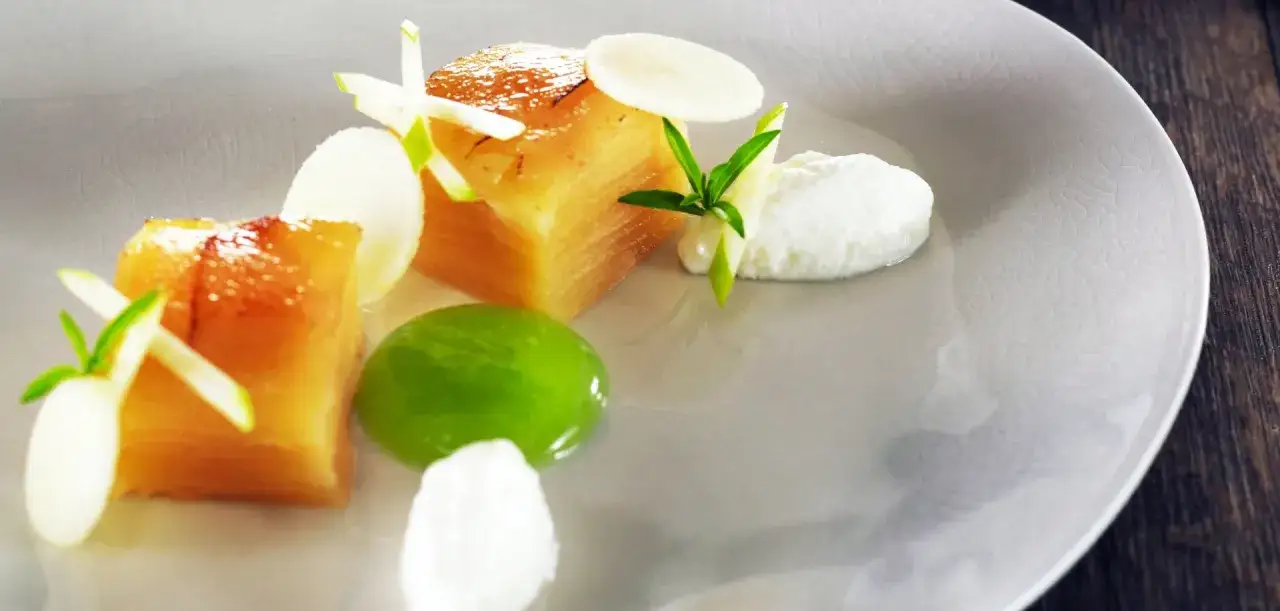 Un délicieux dessert fevrier : cubes de fruits caramélisés, crème fouettée, gelée verte et fines lamelles de pomme sur une assiette texturée.