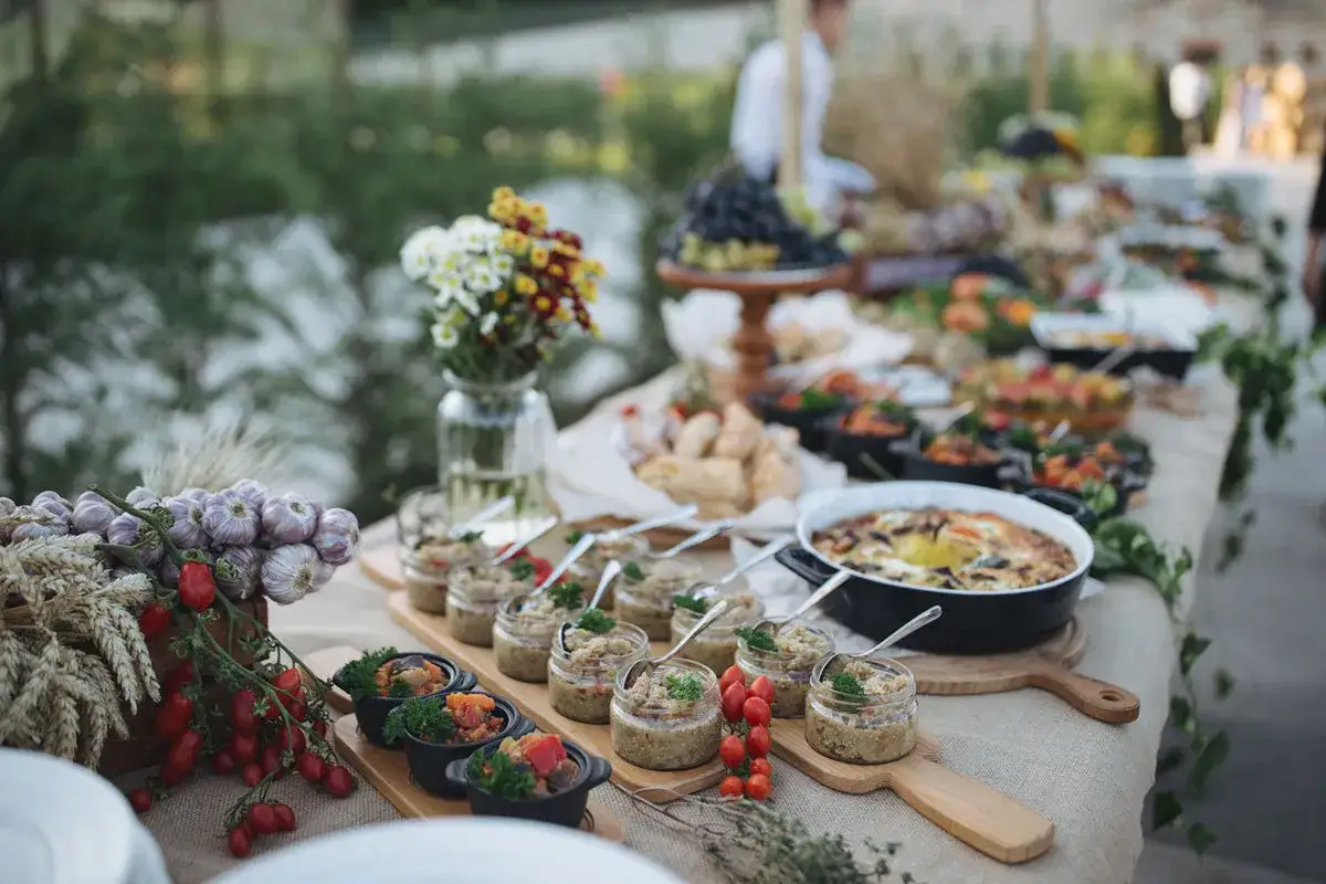 Un buffet baptême chic en extérieur, avec des verrines, des plats chauds, des légumes frais et des fleurs.