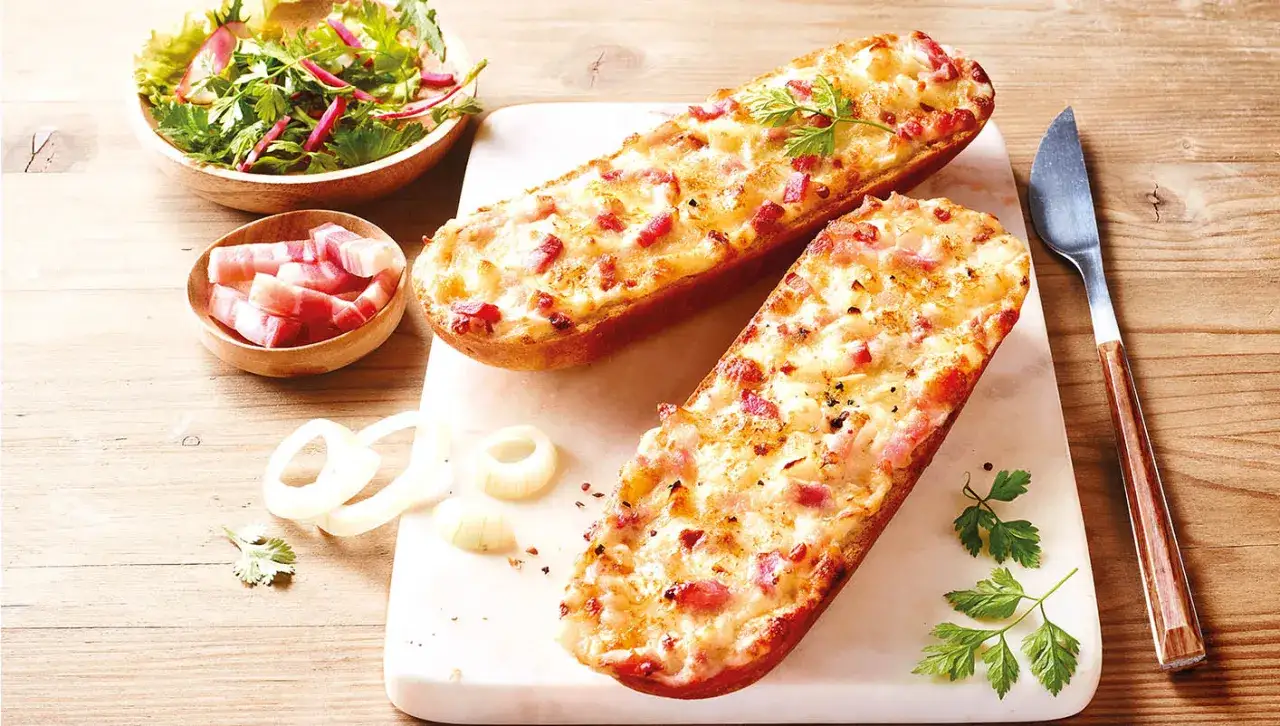 Deux tartines alsaciennes dorées, garnies de lardons et fromage fondant, accompagnées d'une salade fraîche et d'oignons.