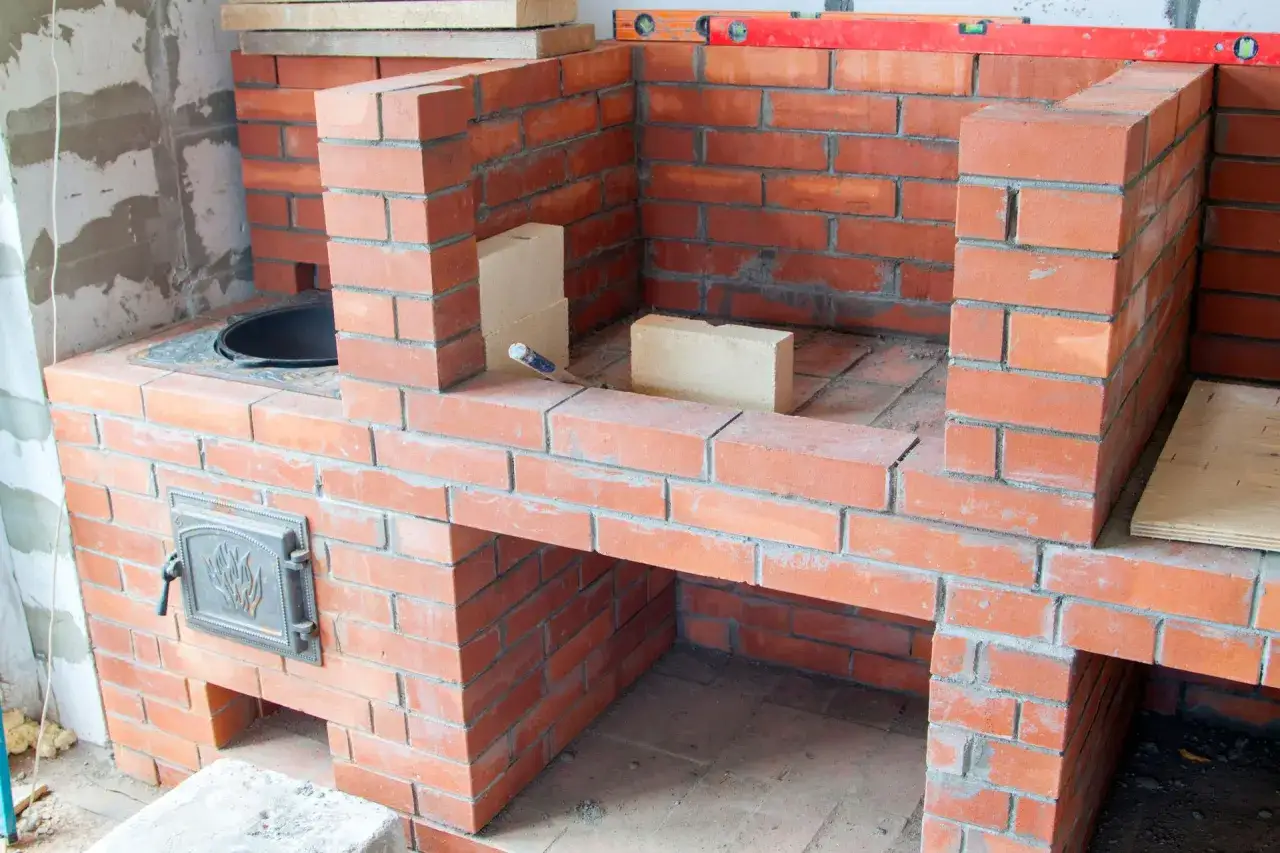 Construction d'un barbecue en briques avec cheminée. Le plan prend forme, les briques rouges s'assemblent pour créer un espace de cuisson fonctionnel.