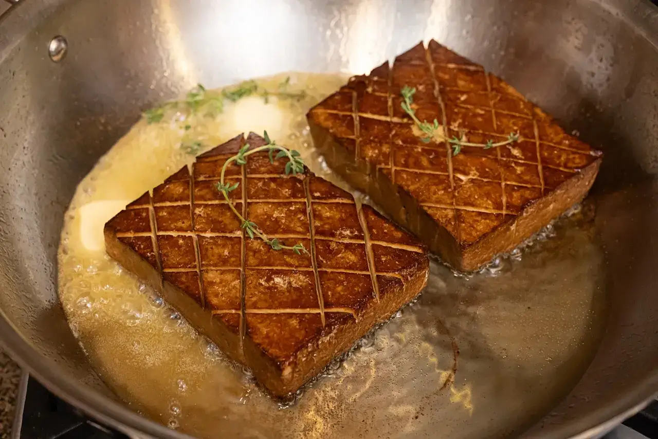 Deux steaks de tofu grill&eacute;s, parfaits pour une recette steak v&eacute;g&eacute;tarien, mijotent dans du beurre avec du thym dans une po&ecirc;le.