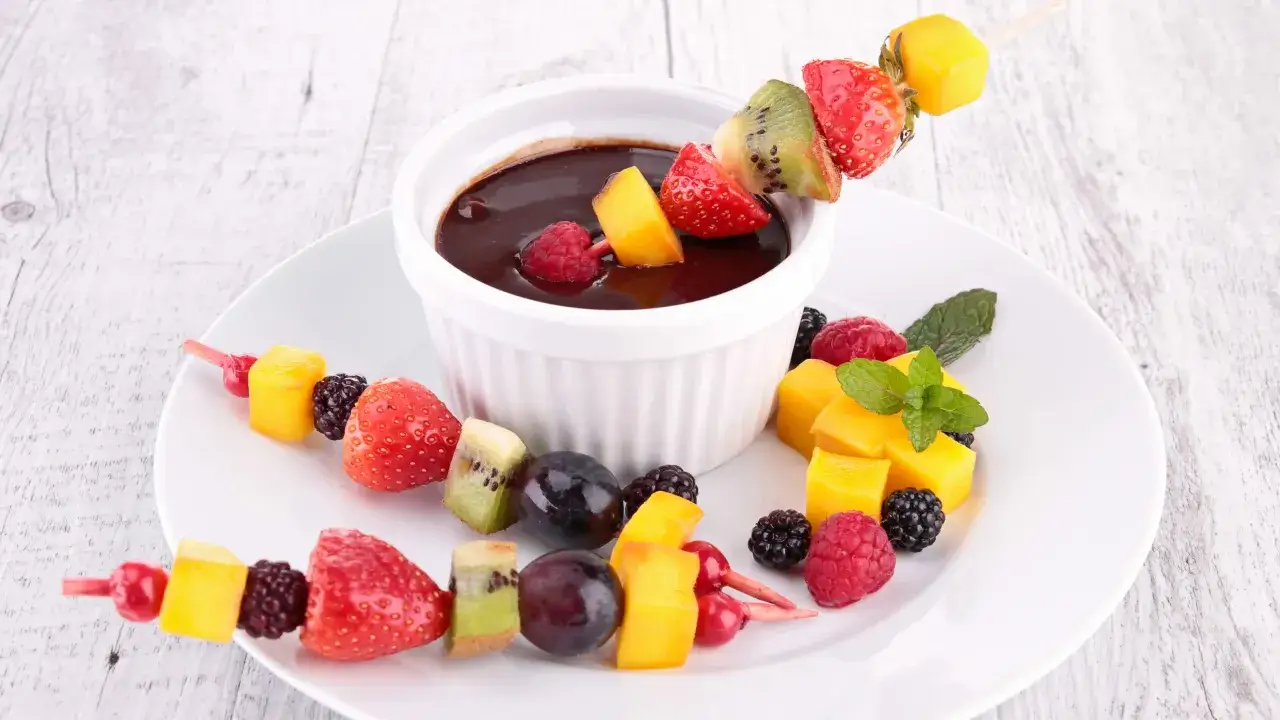Brochettes de fruits frais (fraises, kiwis, mangues, raisins, mûres, framboises) trempées dans une sauce au chocolat, un dessert pour barbecue parfait.