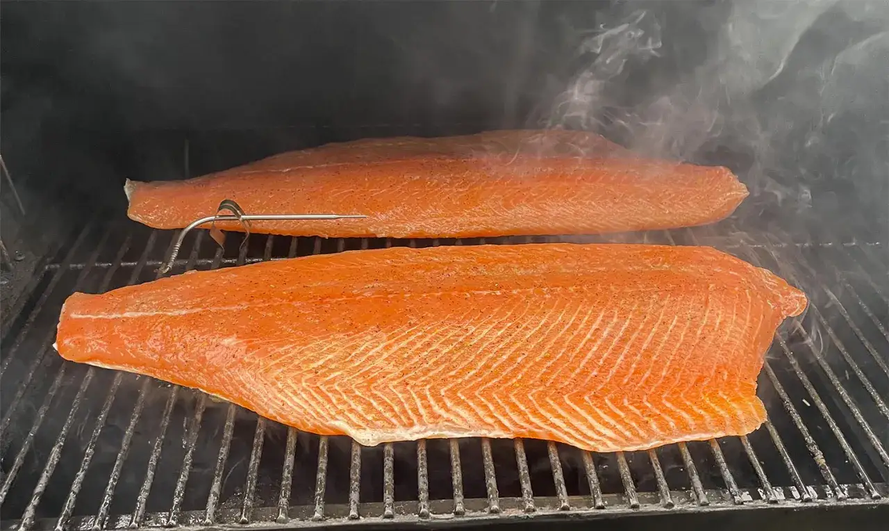 Deux beaux filets de saumon sur une grille, en plein fumage à froid. La fumée légère et les épices promettent un délice.