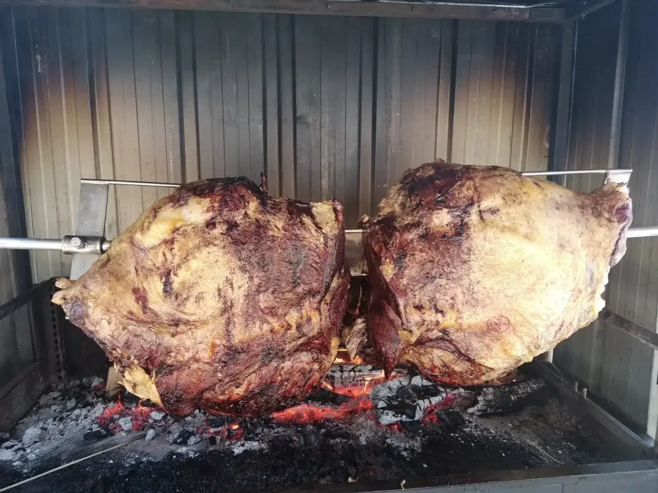 Deux énormes pièces de quelle viande au tourne broche, grillant lentement au-dessus des braises ardentes.