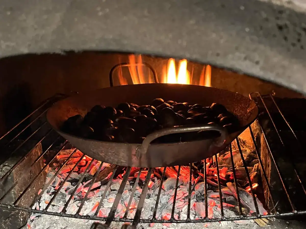 Poêle de châtaignes au barbecue, grésillant sur les braises ardentes sous une douce chaleur de feu.