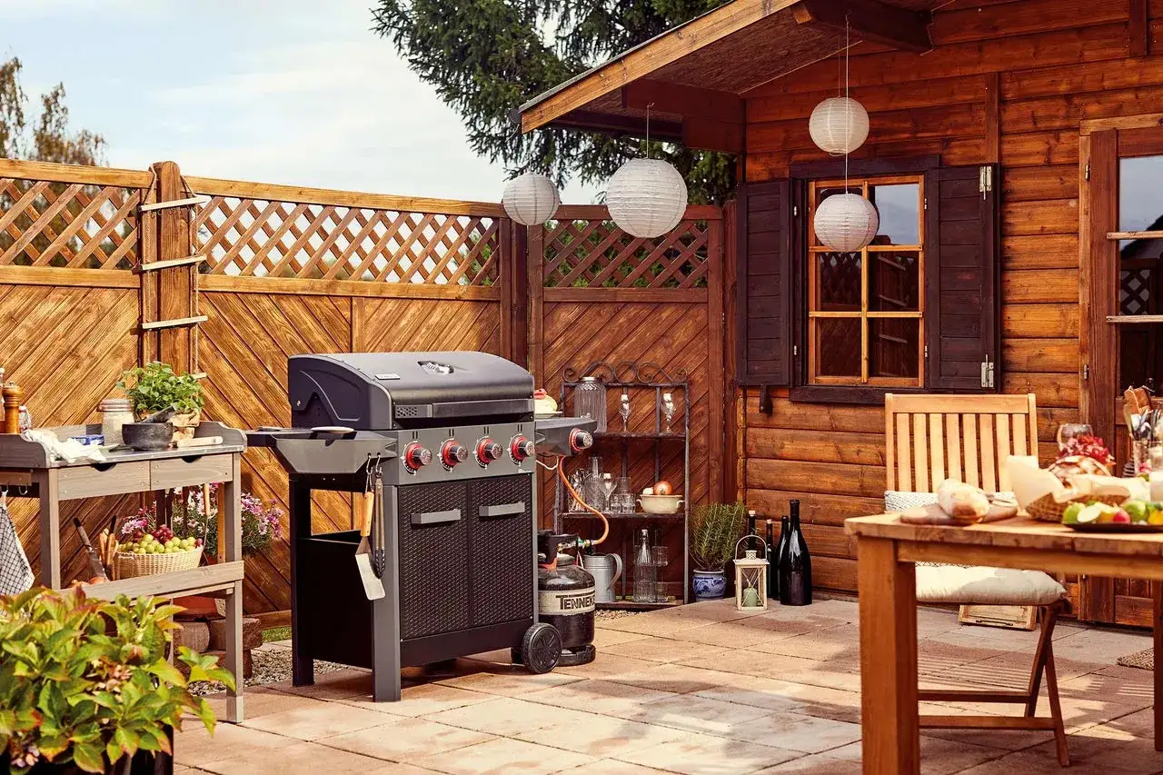 Un coin barbecue couvert, idéal pour fabriquer un espace convivial. Un barbecue à gaz, une table de préparation et une table à manger sont prêts pour un repas en plein air.