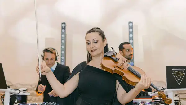 Une violoniste joue lors d'un mariage, avec des DJs en arrière-plan. Un prix DJ mariage pour une ambiance unique.