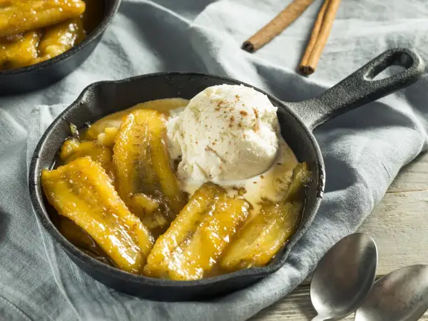 Bananes flambées au barbecue, servies chaudes dans une poêle en fonte avec une boule de glace à la vanille saupoudrée de cannelle.
